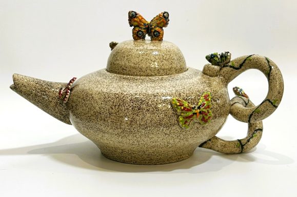 Speckled clay base teapot. Hand painted butterfly and vine 3D appliques. Clear glaze coating. H-5.5in x W-10in.